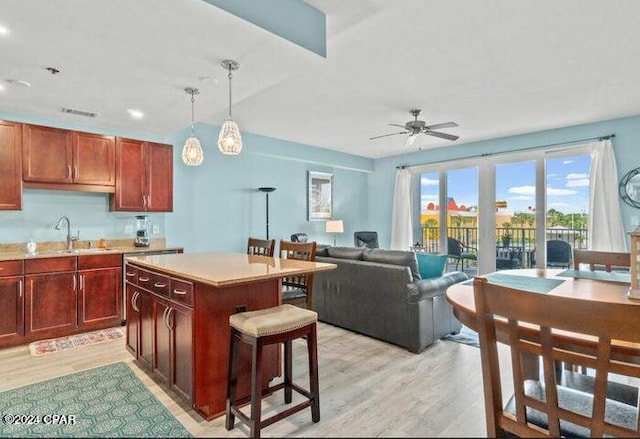 kitchen featuring decorative light fixtures, ceiling fan, sink, a kitchen island, and light hardwood / wood-style floors