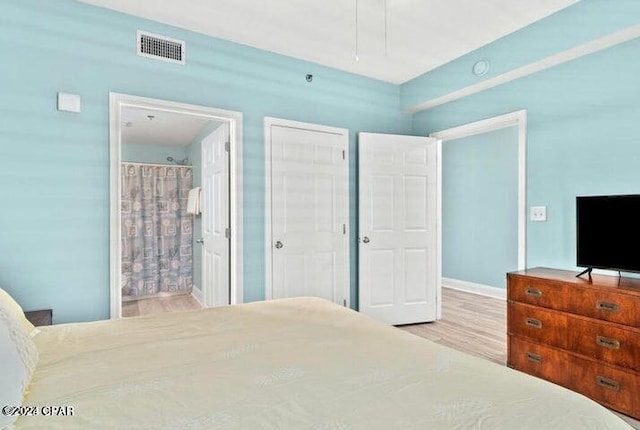 bedroom featuring ensuite bath, visible vents, and wood finished floors