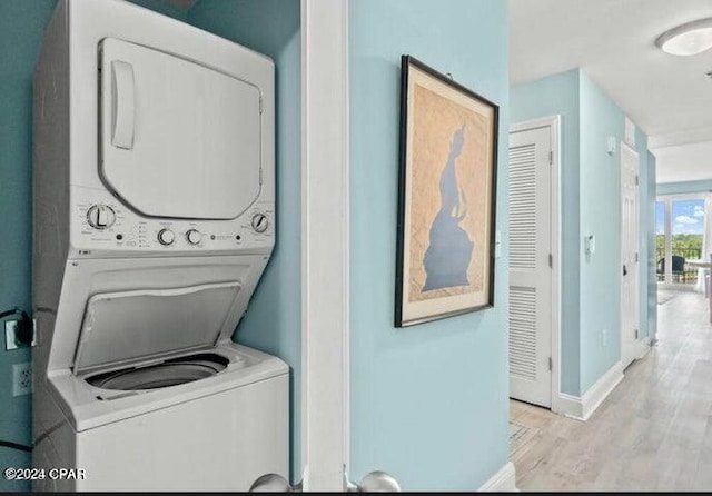 laundry room with baseboards, laundry area, wood finished floors, and stacked washer / drying machine