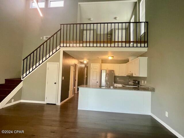 kitchen featuring white cabinets, black stove, dark hardwood / wood-style floors, stainless steel fridge, and kitchen peninsula