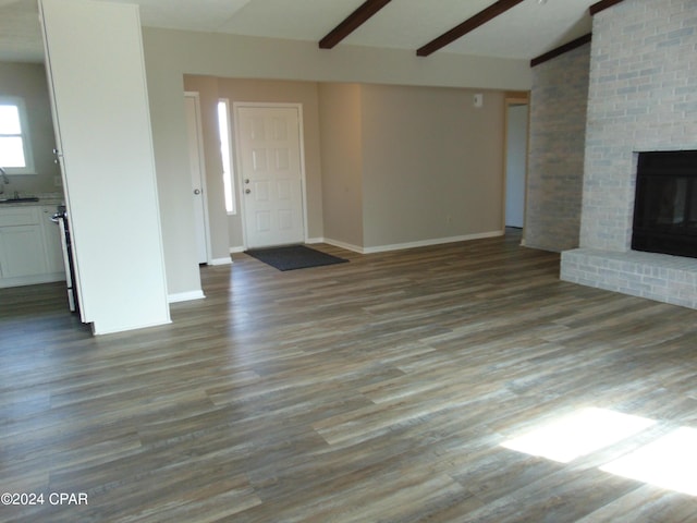 unfurnished living room featuring hardwood / wood-style flooring, sink, beamed ceiling, and a brick fireplace