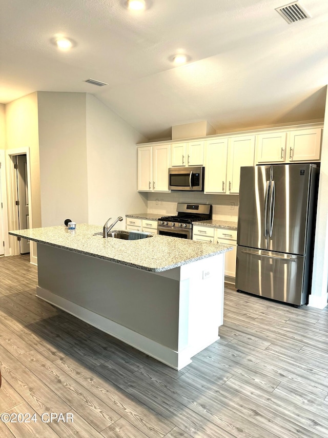 kitchen with a kitchen island with sink, white cabinets, vaulted ceiling, light hardwood / wood-style floors, and stainless steel appliances