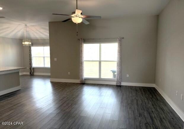 spare room featuring plenty of natural light, ceiling fan with notable chandelier, and dark hardwood / wood-style floors