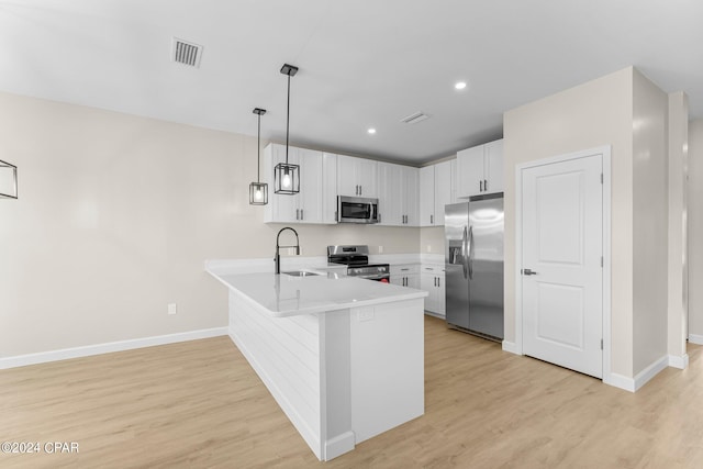 kitchen featuring stainless steel appliances, hanging light fixtures, light wood-type flooring, and kitchen peninsula