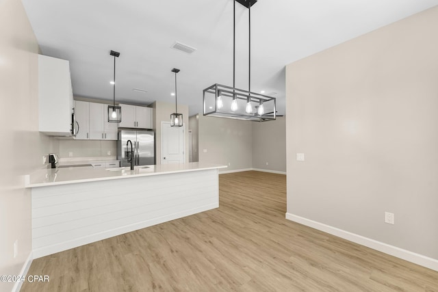 kitchen featuring range, stainless steel fridge, decorative light fixtures, light wood-type flooring, and white cabinetry