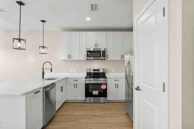 kitchen with decorative light fixtures, sink, appliances with stainless steel finishes, light hardwood / wood-style flooring, and kitchen peninsula