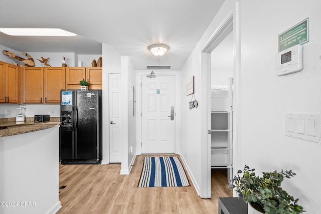 kitchen featuring black fridge with ice dispenser, light hardwood / wood-style floors, and stone countertops