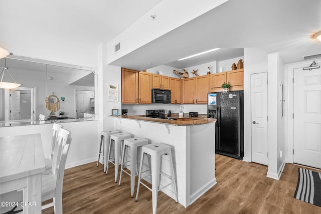 kitchen featuring dark stone countertops, black appliances, hardwood / wood-style flooring, and kitchen peninsula