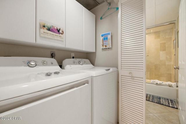 clothes washing area featuring light tile patterned floors, washer and dryer, and cabinets