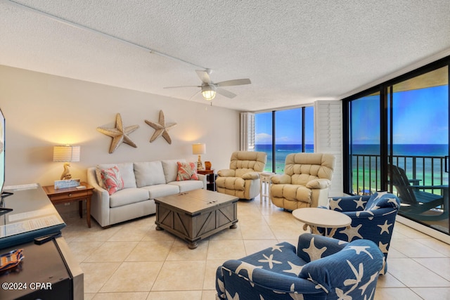 living room with light tile patterned flooring, a water view, a textured ceiling, and ceiling fan