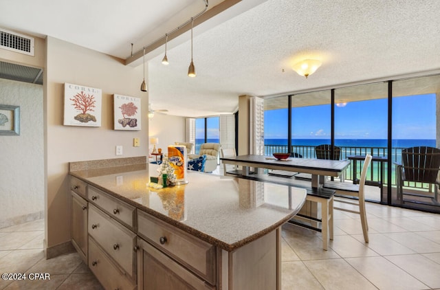 kitchen with light tile patterned flooring, a water view, a wall of windows, track lighting, and stone countertops