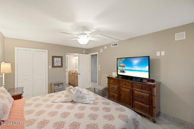 bedroom with ensuite bathroom, a closet, light tile patterned floors, a textured ceiling, and ceiling fan