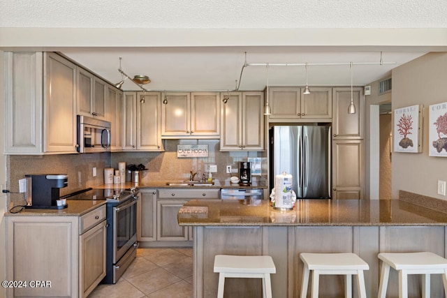 kitchen with dark stone counters, light tile patterned flooring, sink, appliances with stainless steel finishes, and kitchen peninsula