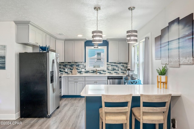 kitchen featuring gray cabinetry, light countertops, decorative backsplash, appliances with stainless steel finishes, and light wood-style floors