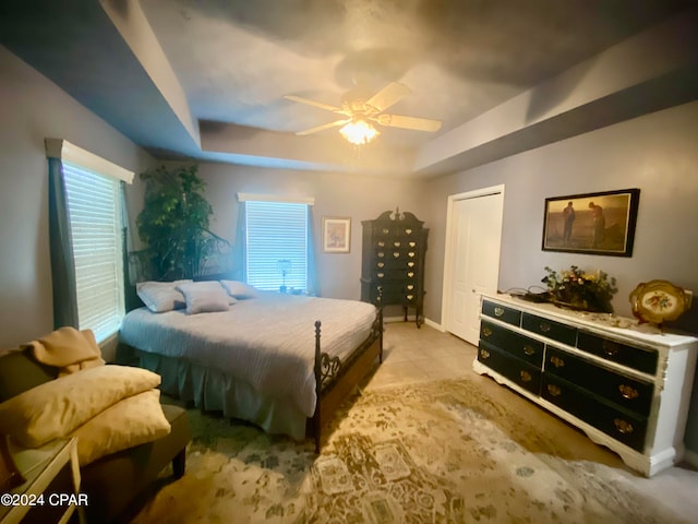 tiled bedroom featuring a closet, ceiling fan, and a raised ceiling