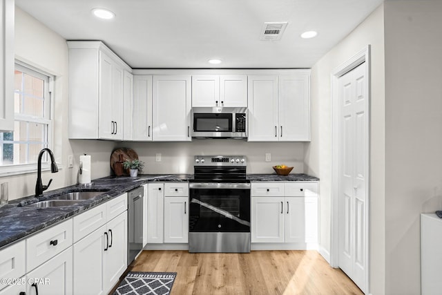 kitchen with white cabinets, appliances with stainless steel finishes, dark stone countertops, sink, and light wood-type flooring