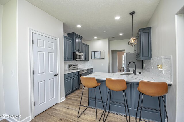 kitchen with appliances with stainless steel finishes, tasteful backsplash, kitchen peninsula, light stone counters, and light wood-type flooring