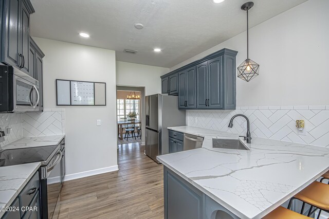 kitchen featuring hanging light fixtures, stainless steel appliances, sink, and light stone countertops