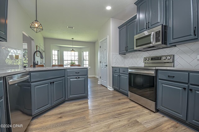 kitchen featuring stainless steel appliances, decorative light fixtures, and light hardwood / wood-style floors