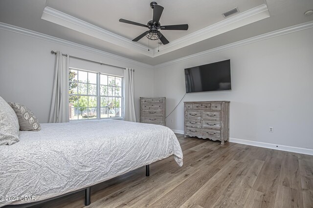 bedroom with a tray ceiling, ornamental molding, hardwood / wood-style floors, and ceiling fan