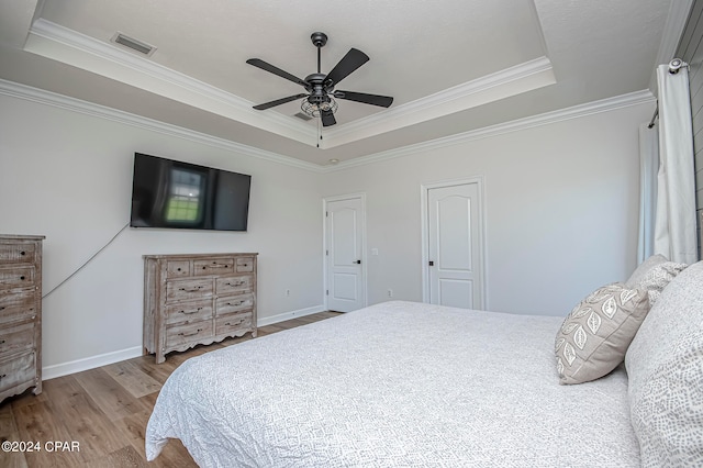 bedroom featuring light hardwood / wood-style floors, a raised ceiling, crown molding, and ceiling fan