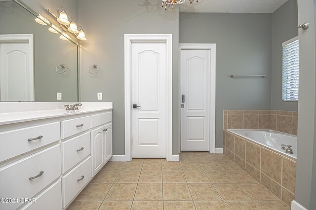 bathroom with tile patterned flooring, a relaxing tiled tub, and vanity