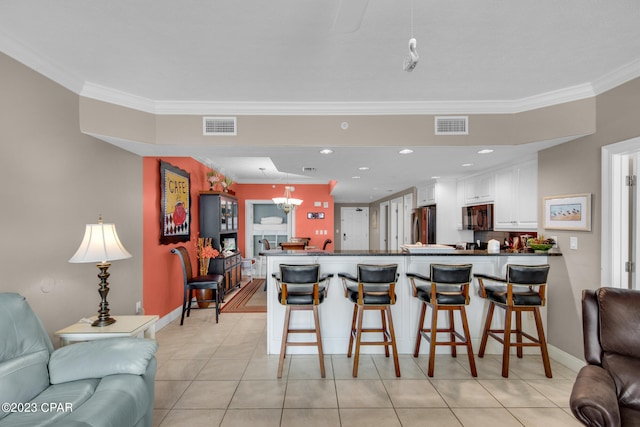 kitchen with light tile patterned floors, a kitchen bar, crown molding, kitchen peninsula, and white cabinetry