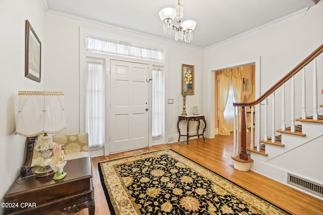 foyer entrance with hardwood / wood-style flooring, crown molding, and an inviting chandelier