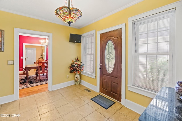 entryway with light tile patterned flooring, ornamental molding, and a notable chandelier