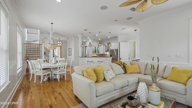 living room featuring ceiling fan with notable chandelier, light hardwood / wood-style flooring, and crown molding