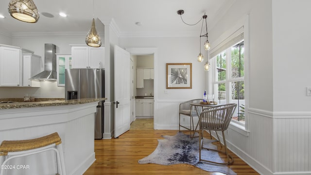 kitchen with light hardwood / wood-style floors, crown molding, hanging light fixtures, white cabinets, and wall chimney exhaust hood