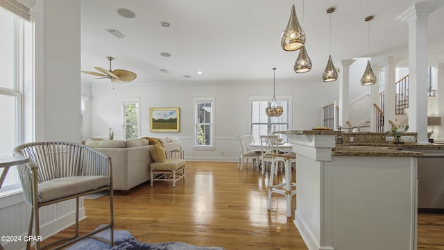 kitchen with decorative light fixtures, wood-type flooring, dark stone countertops, ceiling fan, and decorative columns