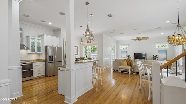 kitchen featuring white cabinets, appliances with stainless steel finishes, decorative light fixtures, wall chimney range hood, and ceiling fan