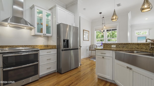 kitchen with appliances with stainless steel finishes, decorative light fixtures, dark stone counters, wall chimney exhaust hood, and white cabinets