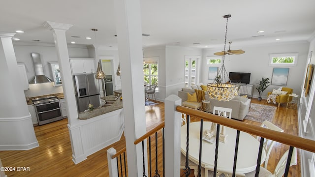 interior space with appliances with stainless steel finishes, wall chimney exhaust hood, white cabinetry, and light hardwood / wood-style floors