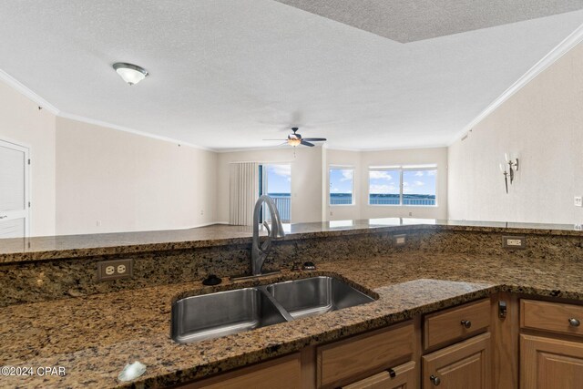 kitchen featuring a textured ceiling, crown molding, dark stone countertops, and sink