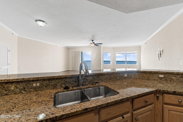 kitchen with ceiling fan, a textured ceiling, a sink, ornamental molding, and dark stone counters