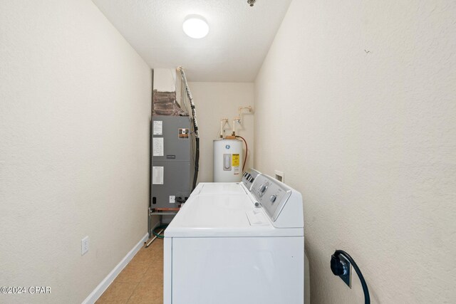 washroom with a textured ceiling, electric water heater, heating unit, washer and clothes dryer, and light tile patterned flooring