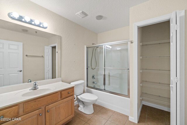 full bathroom with tile patterned flooring, combined bath / shower with glass door, a textured ceiling, toilet, and vanity