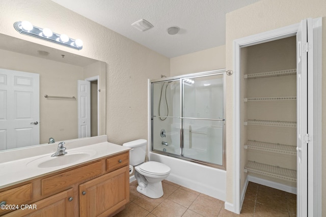 bathroom featuring a textured ceiling, tile patterned flooring, toilet, vanity, and combined bath / shower with glass door