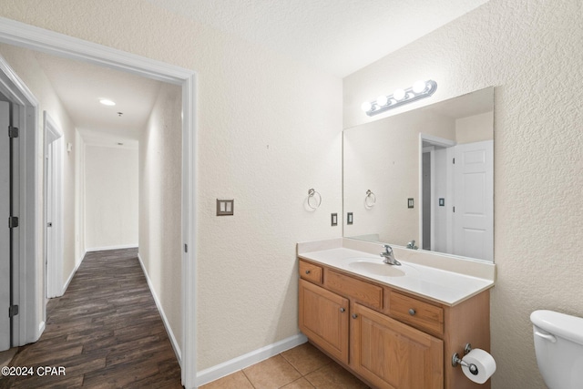 bathroom with a textured wall, vanity, toilet, and baseboards