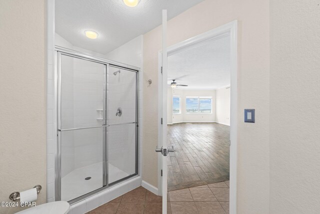 bathroom featuring ceiling fan, a shower with door, wood-type flooring, and a textured ceiling