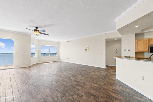 unfurnished living room with ceiling fan, dark wood-type flooring, a textured ceiling, a water view, and ornamental molding