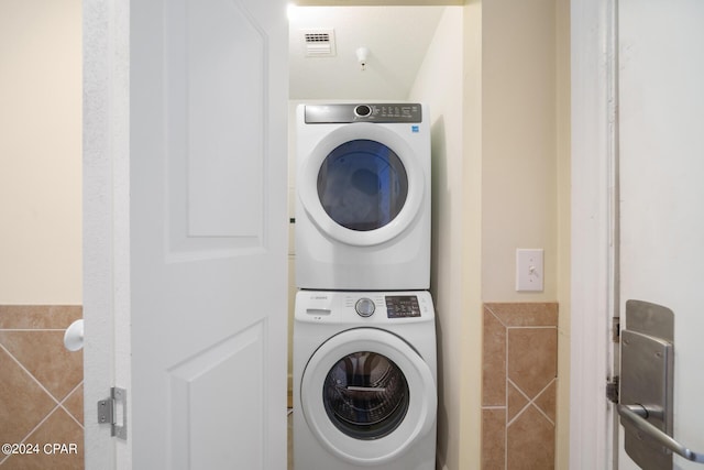 washroom with stacked washing maching and dryer and tile walls