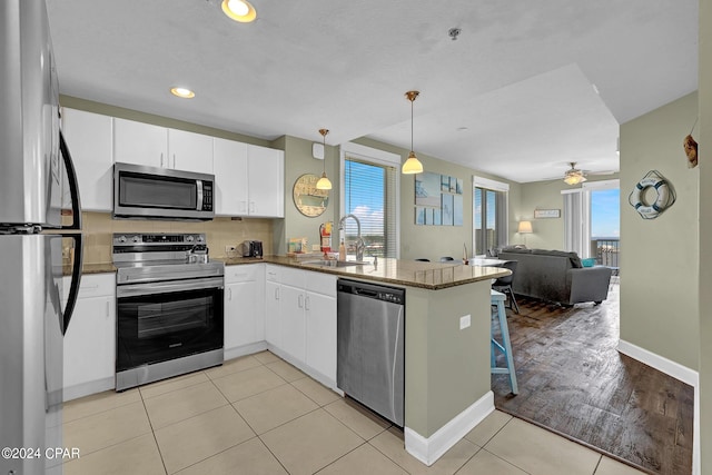 kitchen featuring a peninsula, white cabinets, open floor plan, appliances with stainless steel finishes, and pendant lighting