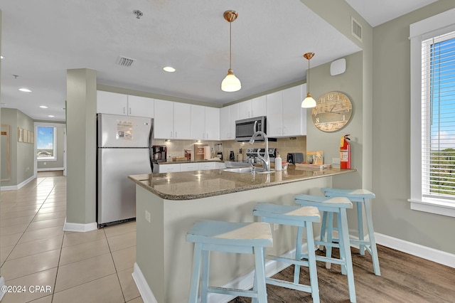 kitchen featuring white cabinets, a peninsula, hanging light fixtures, stainless steel appliances, and a sink