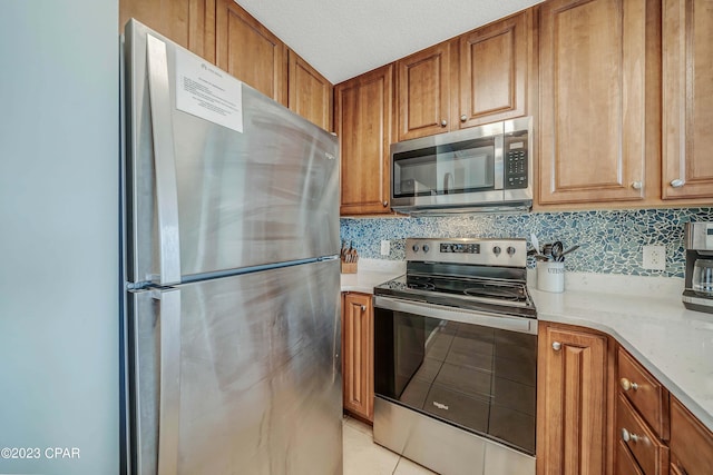 kitchen featuring light tile patterned flooring, appliances with stainless steel finishes, tasteful backsplash, light stone counters, and a textured ceiling