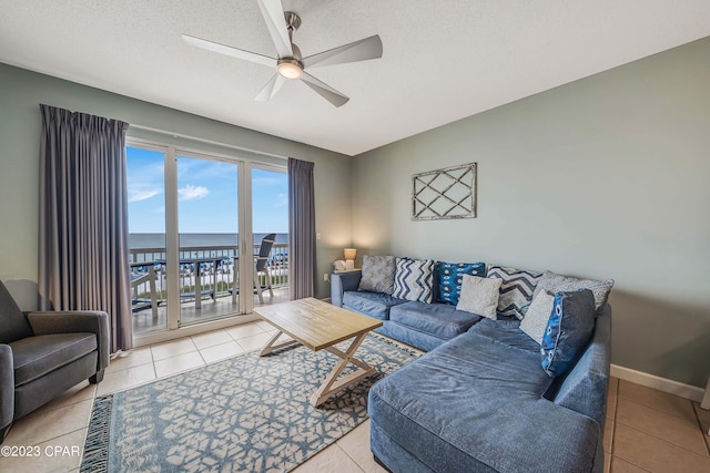 tiled living room with a water view, a textured ceiling, and ceiling fan