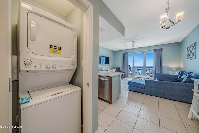 laundry room featuring stacked washer and dryer, light tile patterned flooring, and ceiling fan with notable chandelier