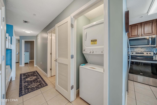 laundry room featuring stacked washing maching and dryer, a textured ceiling, and light tile patterned floors